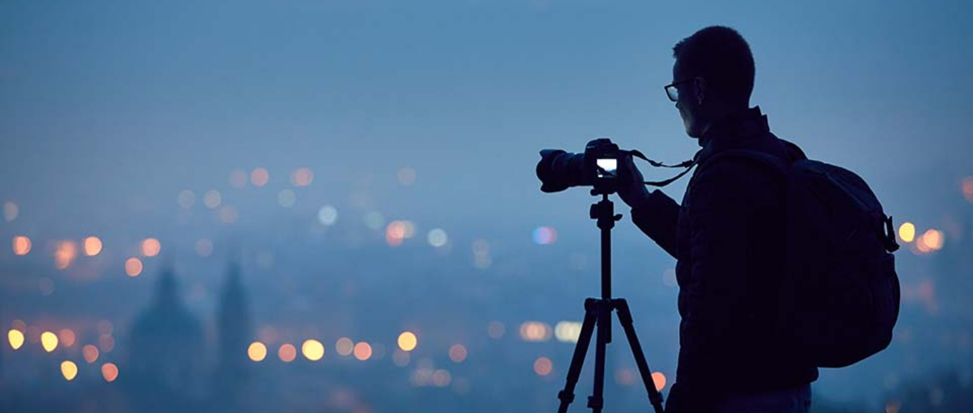 Photographer with camera on tripod against city lights